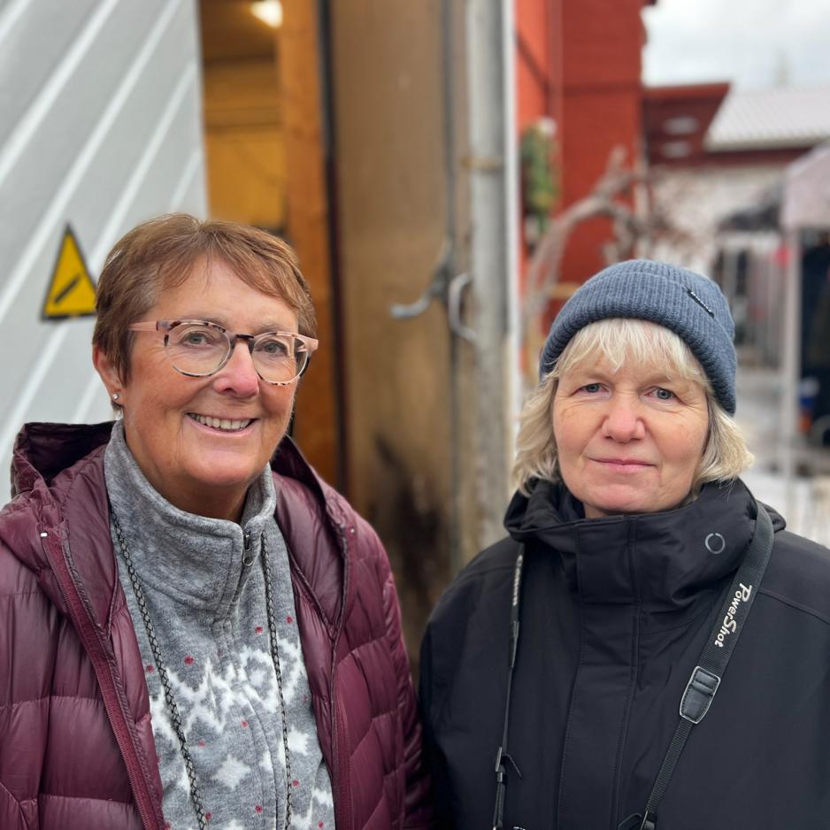 To kvinner som st&aring;r sammen. Anne-Brit til venstre i lilla jakke, brunt kort sveis og briller. Trine Nevrum til h&oslash;yre med hvit pannelugg, svart lue og jakke. Begge smiler