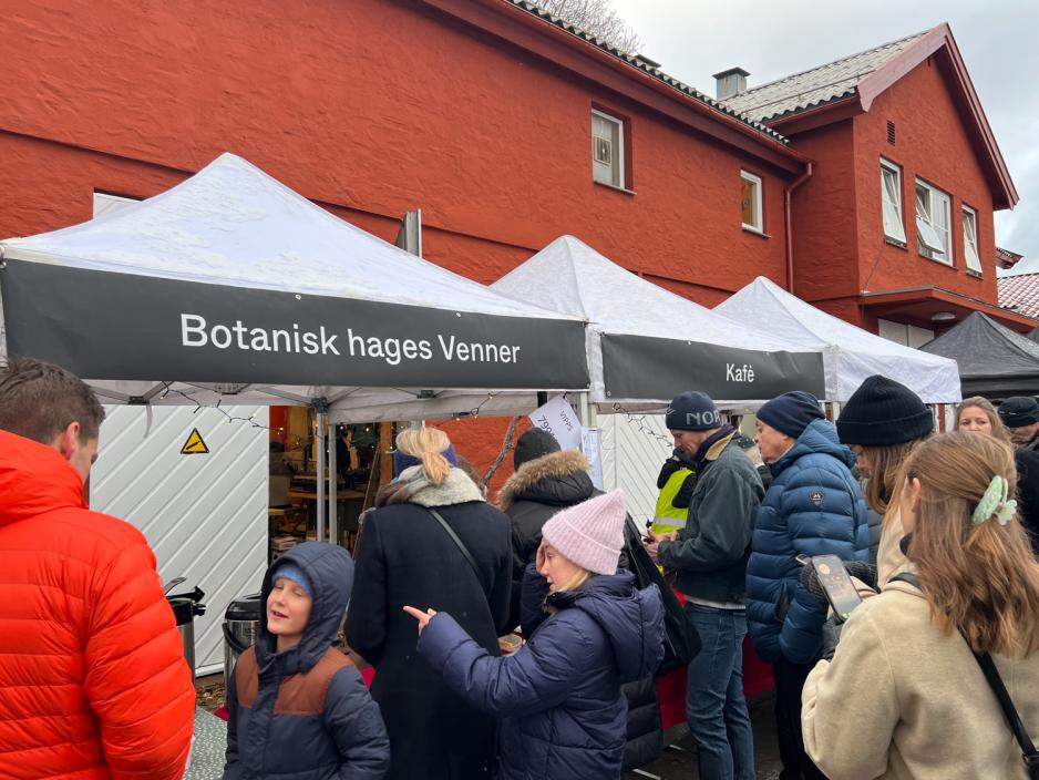 Salgsboder i hvitt telt. Stor tekst der det st&aring;r "botanisk hages venner", folk omkring som kj&oslash;per og snakker sammen