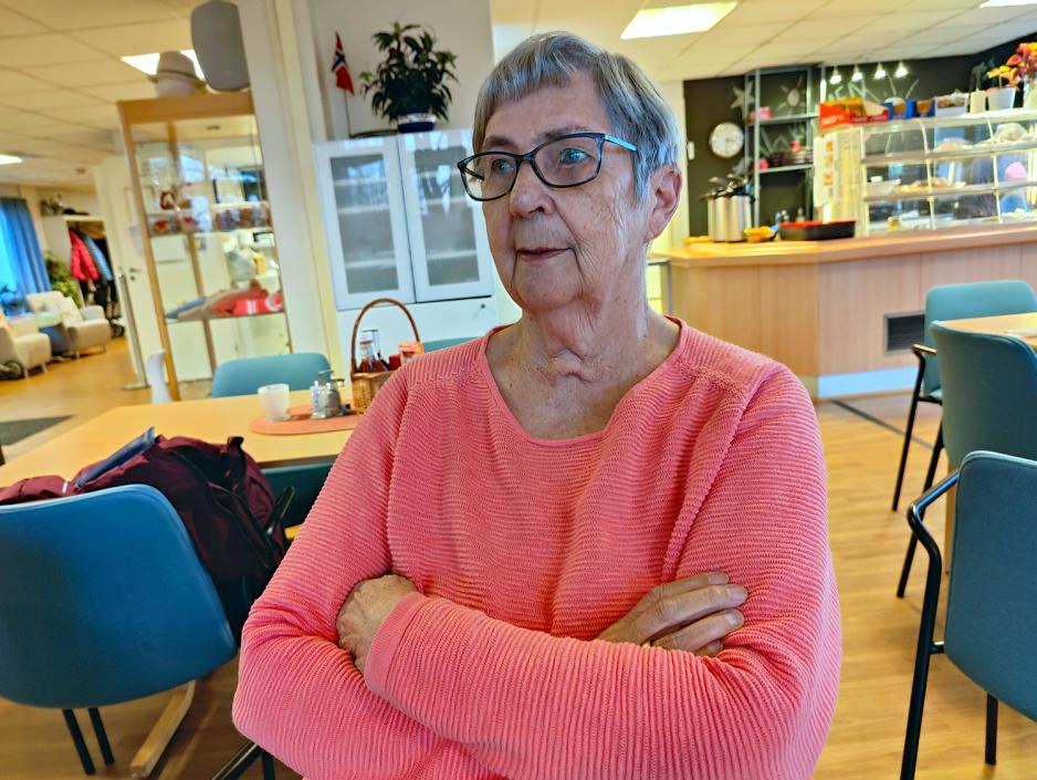 Dame i rosa genser med armene krysset. Briller. Bl&aring; stoler bak. 