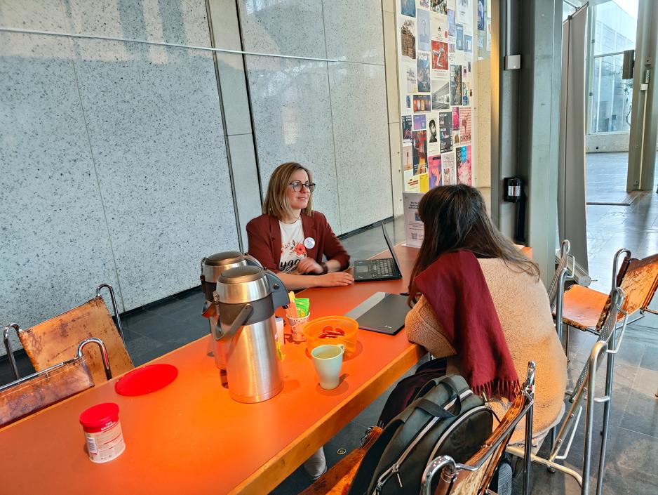 To damer sitter ved et oransje bord. Pepperkaker. Kaffe. Gr&aring; glassbakgrunn.