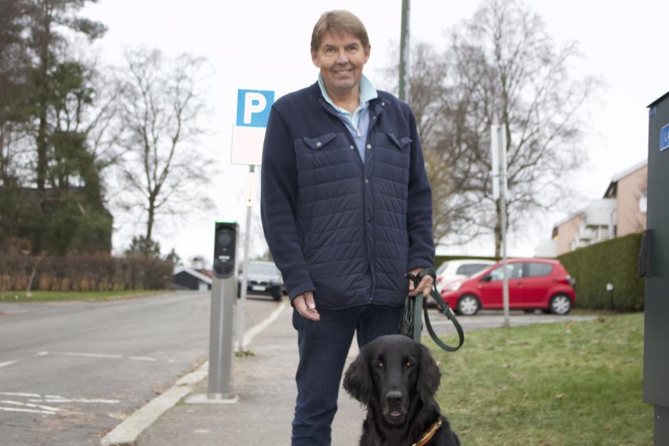 En mann og en svart hund ser rett inn i linsen. De st&aring;r p&aring; fortauet. 