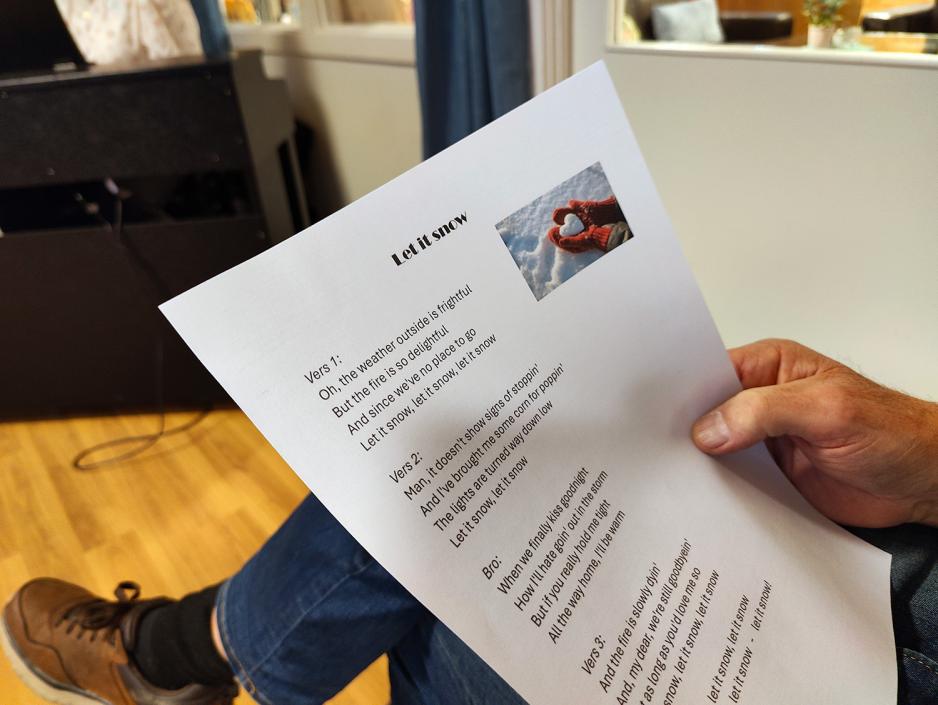 Sangtekst med Let it Snow. Ser en fot I bakken og en h&aring;nd som holder sangen.