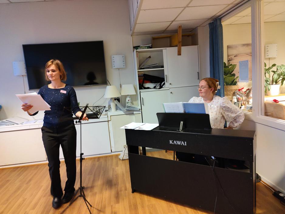 Dame som ser ned p&aring; sangtekst. Dame bak sort piano.