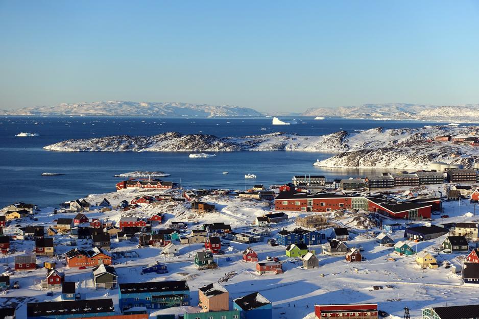Fargerike hus st&aring;r i sn&oslash;dekket landskap. Det er mulig &aring; se hav og fjell