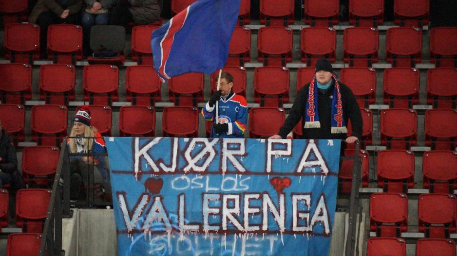En supporter veiver med et flagg fremfor en banner med teksten "Kj&oslash;r p&aring; V&aring;lerenga" 