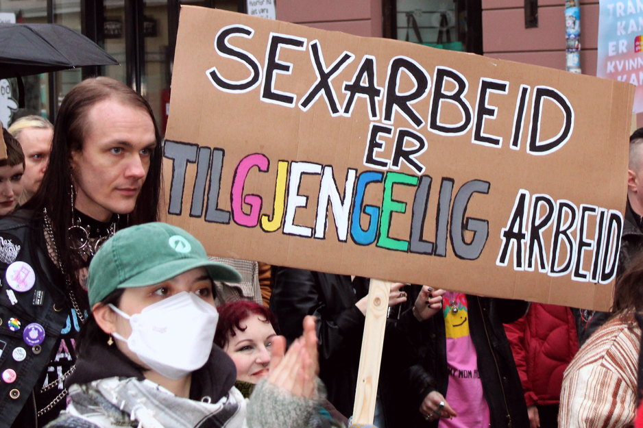 En dame i rullestol l&oslash;fter et skilt der det st&aring;r sexarbeid er tilgjengelig arbeid