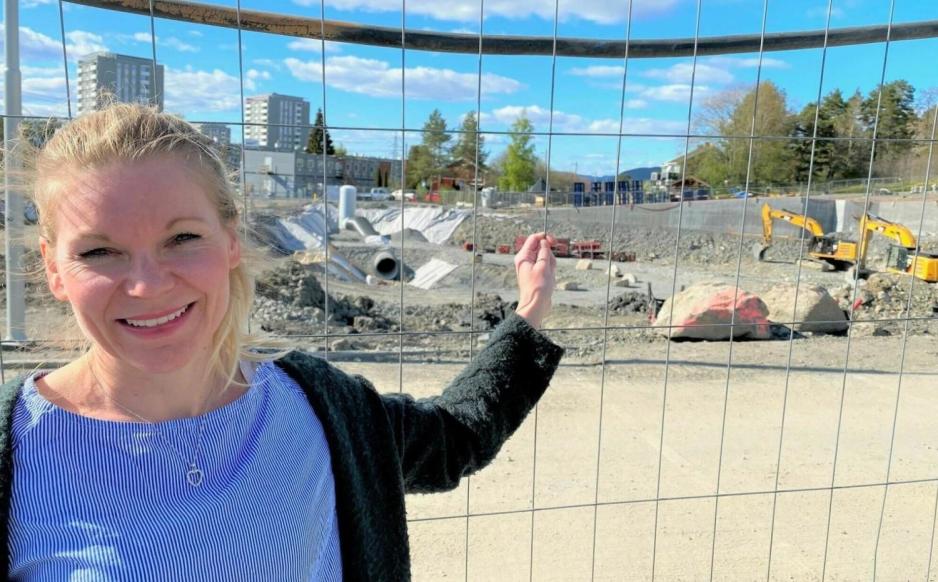 En dame som st&aring;r forran et gjerde og peker p&aring; en graveplass