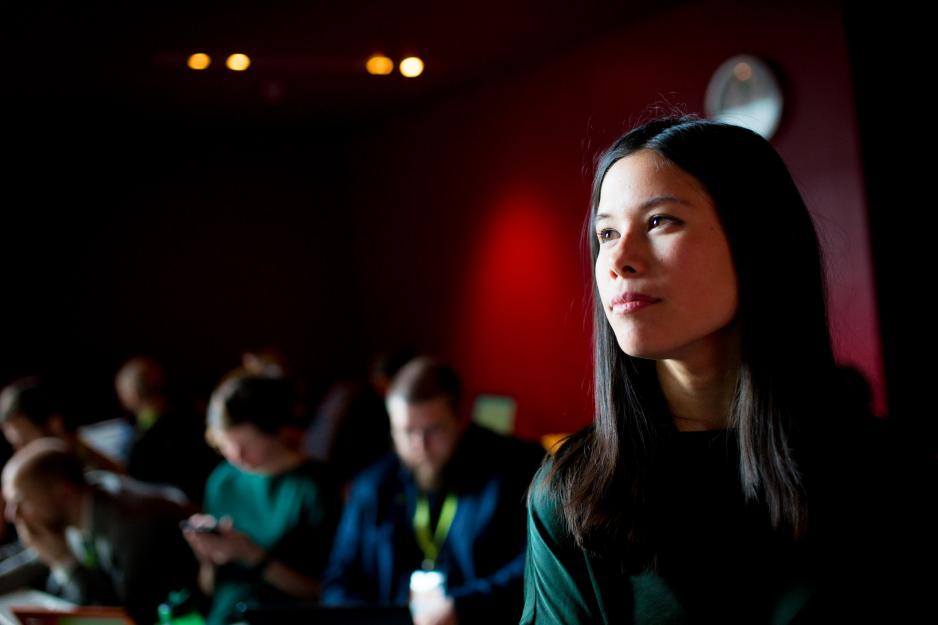 Dame med m&oslash;rkt h&aring;r i forgrunnen til h&oslash;yre i bildet og flere folk i bakgrunnen
