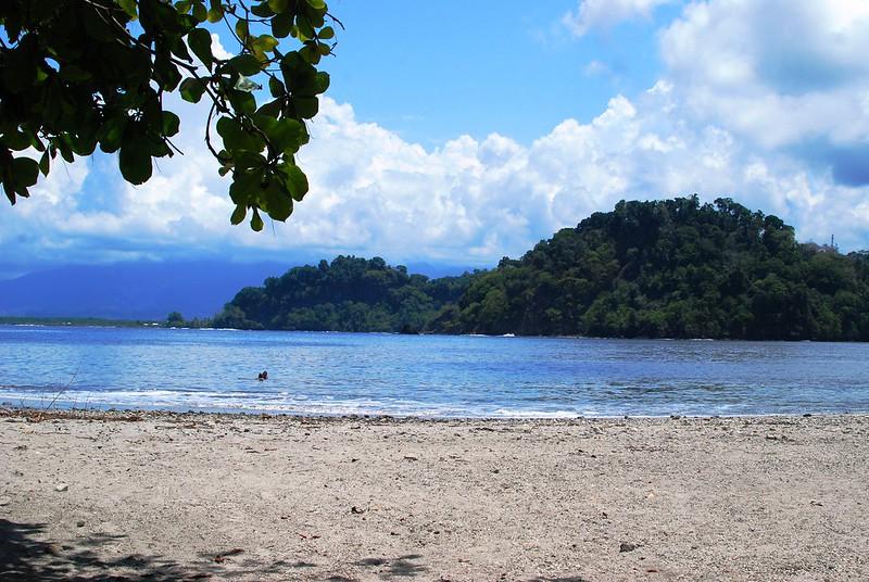 En sandstrand vendt ut mot havet i Costa Rica. Ute i havgapet ser vi en skogkledd &oslash;y.