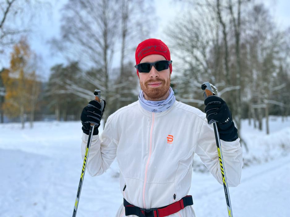 Mann med r&oslash;d lue, solbriller, en tynn treningsjakke og en stav i hver h&aring;nd.