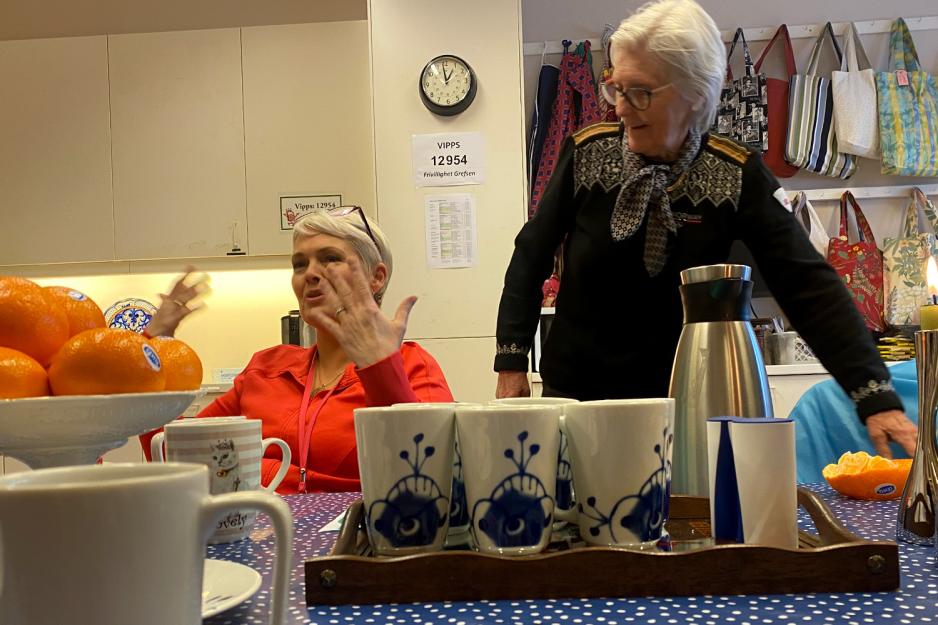 En dame sitter i en stol, en annen er p&aring; vei til &aring; sette seg