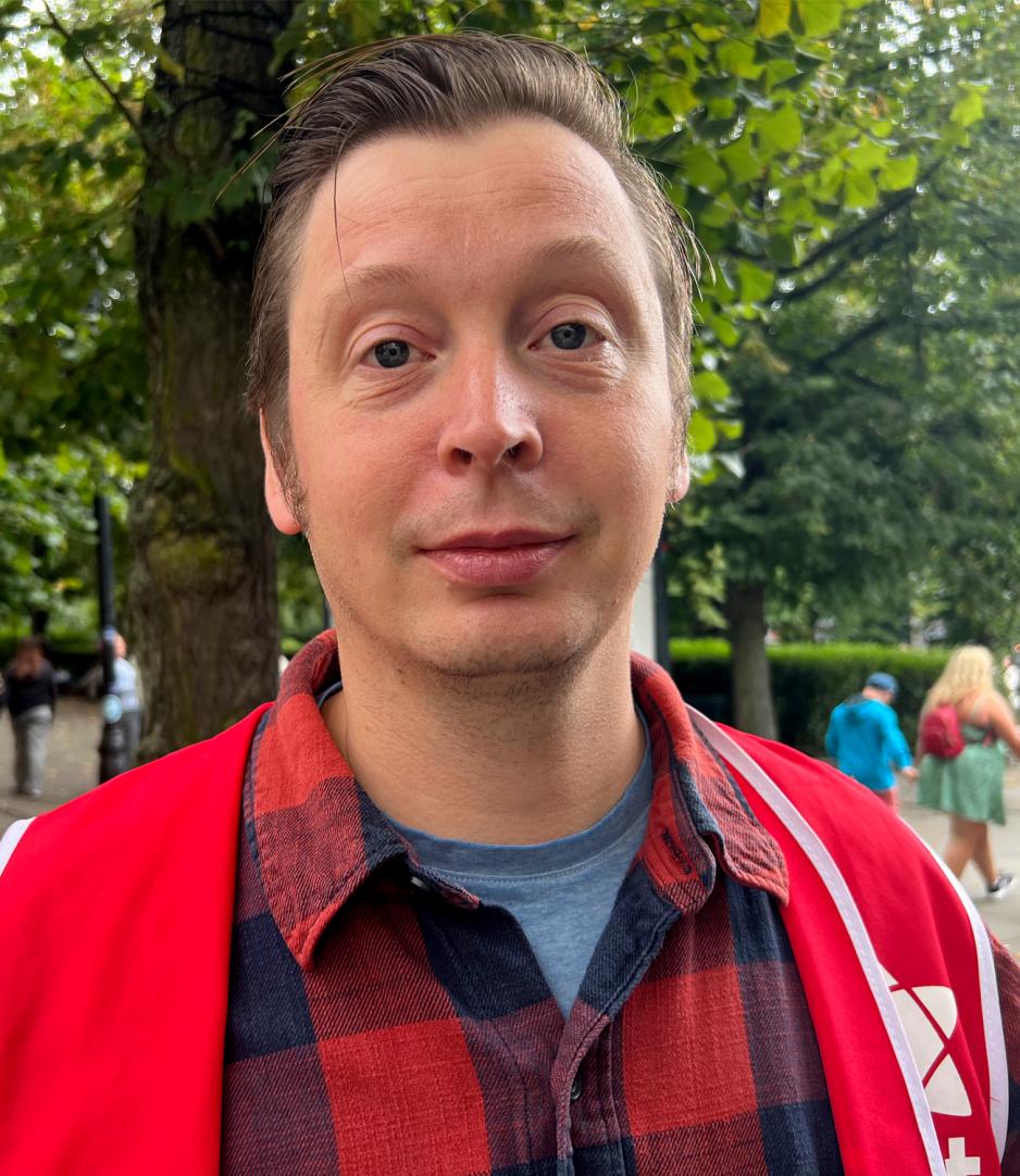 Portrettbilde av B&aring;rd Foller&aring;s, 20. kandidat R&oslash;dt. Kledd i r&oslash;d og svart rutete skjorte og en r&oslash;dt partivest, som ser p&aring; kamera med store &oslash;yne