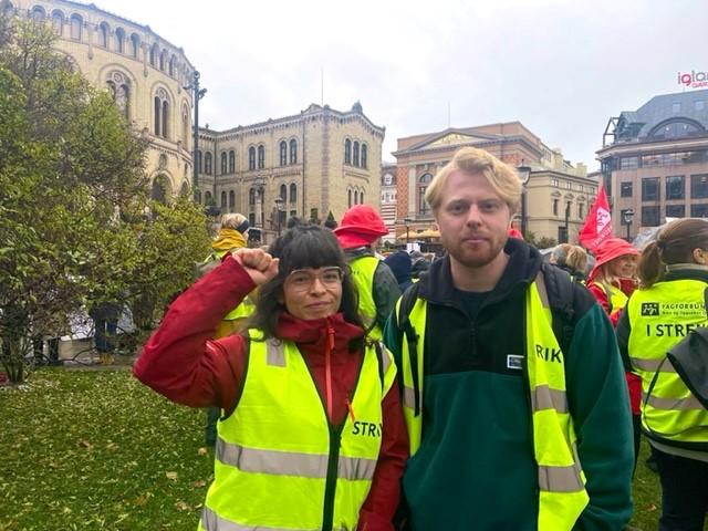 Dame st&aring;r med h&aring;nden hevet og knyttet sammen med mann, foran stor folkemengde i demsonstrasjon.