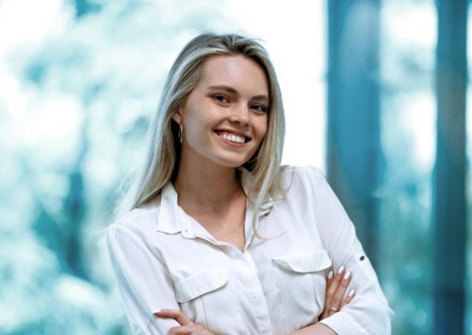 En ung kvinne st&aring;r med hendene i kors og ser smilende mot kamera.
