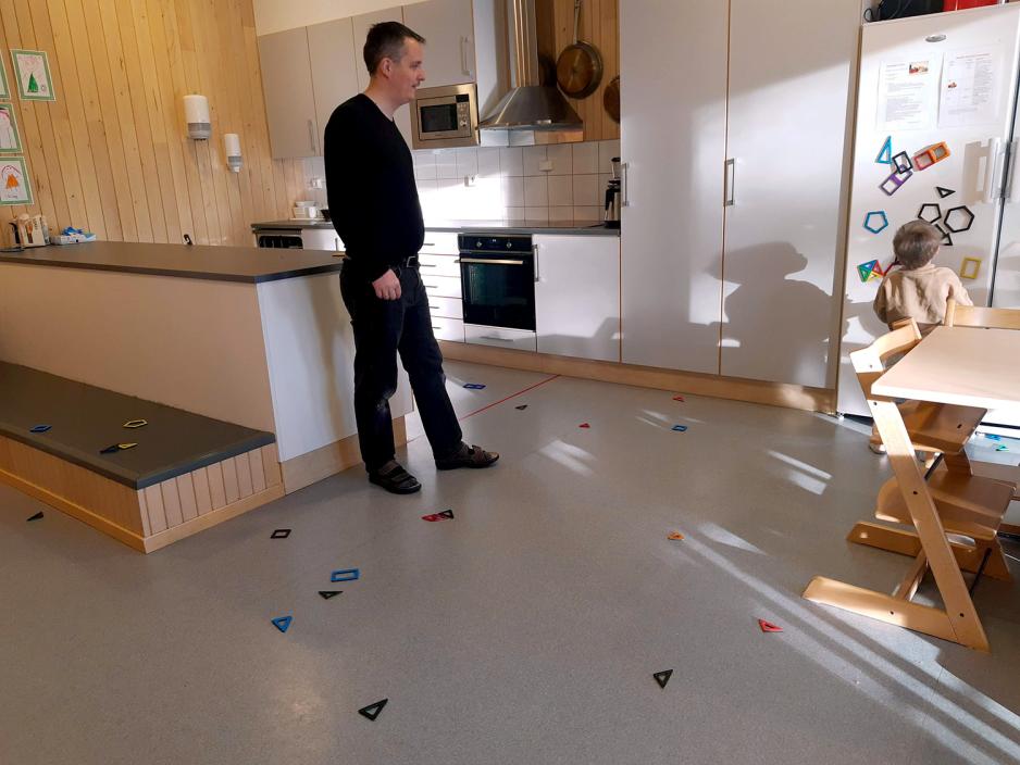Mann st&aring;r og ser p&aring; et barn ta magneter p&aring; kj&oslash;leskapet. Rundt dem ligger mange magneter p&aring; gulvet.