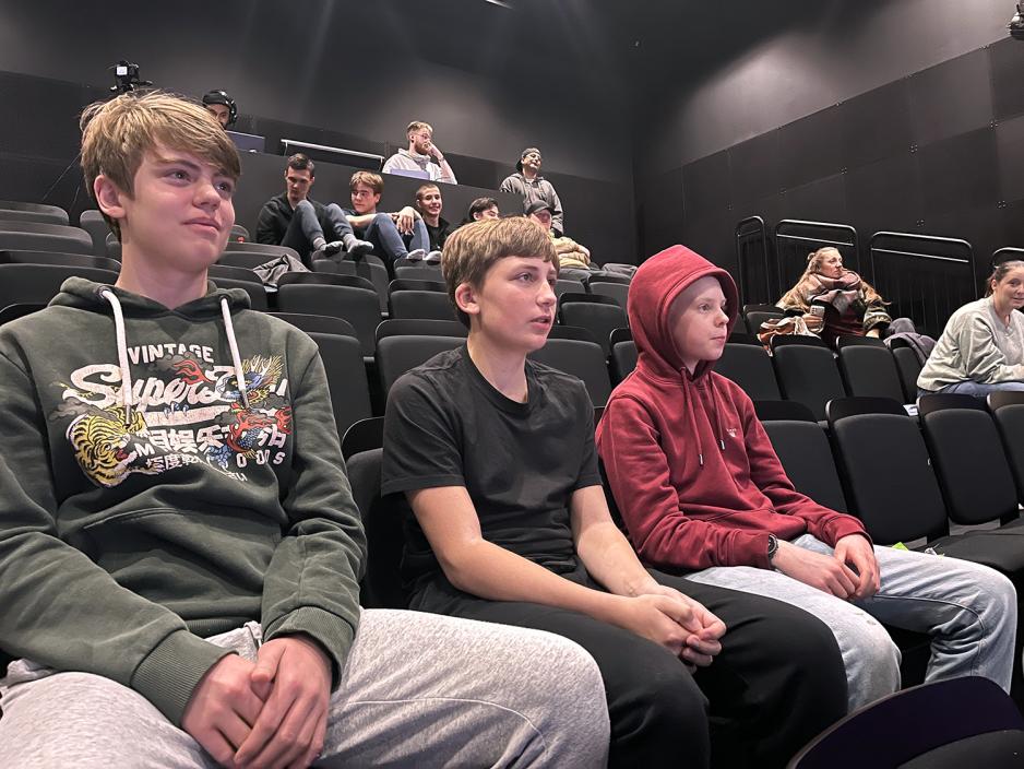 Tre gutter sitter p&aring; en tribune og f&oslash;lger med p&aring; en kamp.