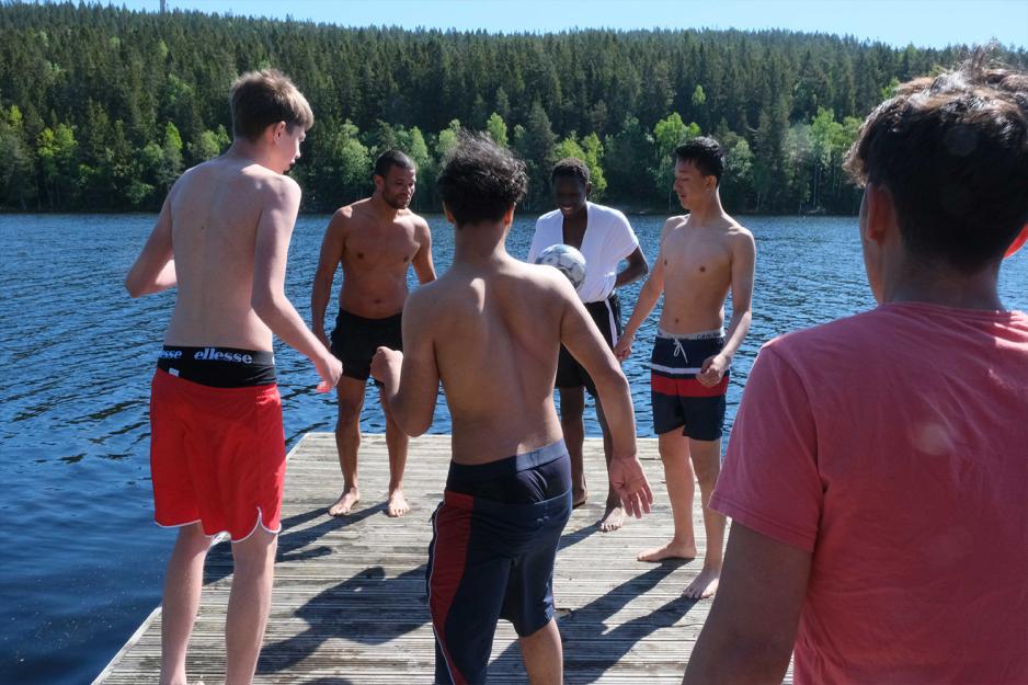 Seks unge gutter st&aring;r i ring p&aring; flytebrygge og spiller enspretten med ball.