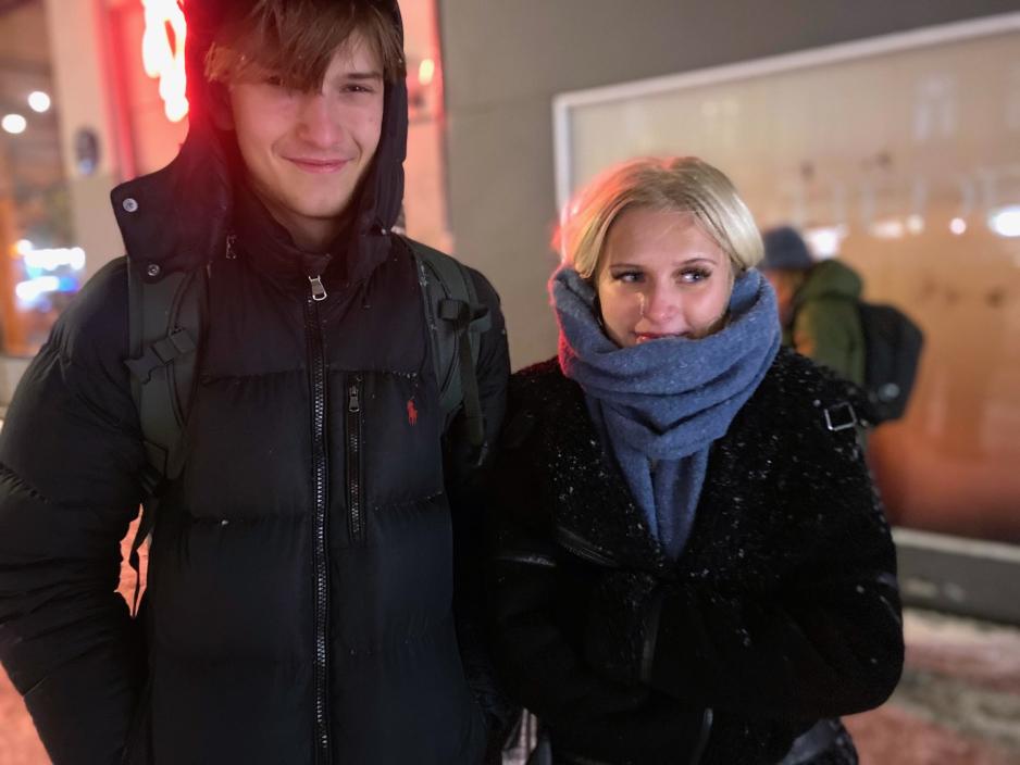 Bildet viser Falk L&oslash;vik-Thue og Constance R&oslash;nning. Begge har p&aring; seg sort jakke, men Constance har et bl&aring;tt skjerf knyttet rundt halsen. Falk smiler til kameraet, mens Constance kikker i retning mot bussen, og holder rundt seg for &aring; f&aring; mer varme. 
