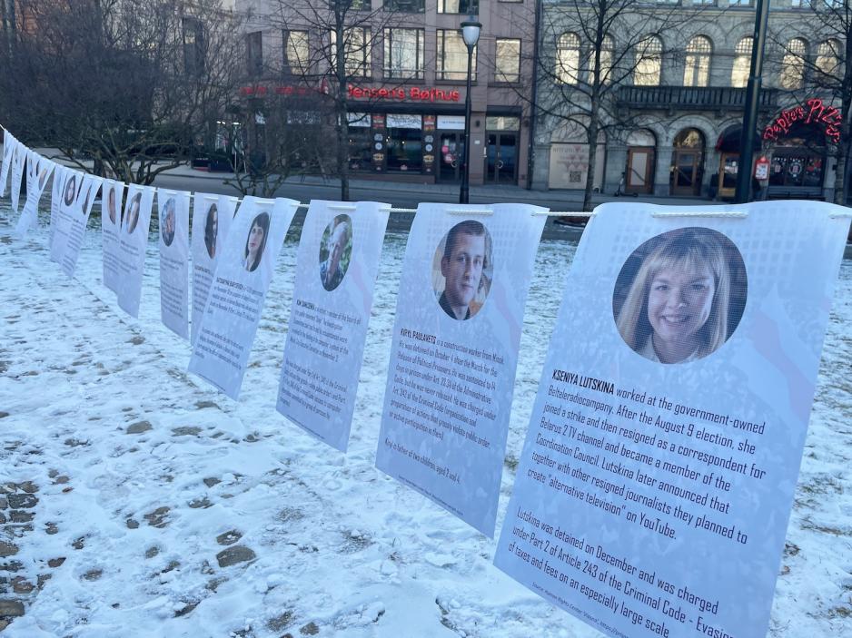 Remse hengt opp p&aring; stang med flere A4 ark, der fengslede demonstranter fra Hviterussland er avbildet.