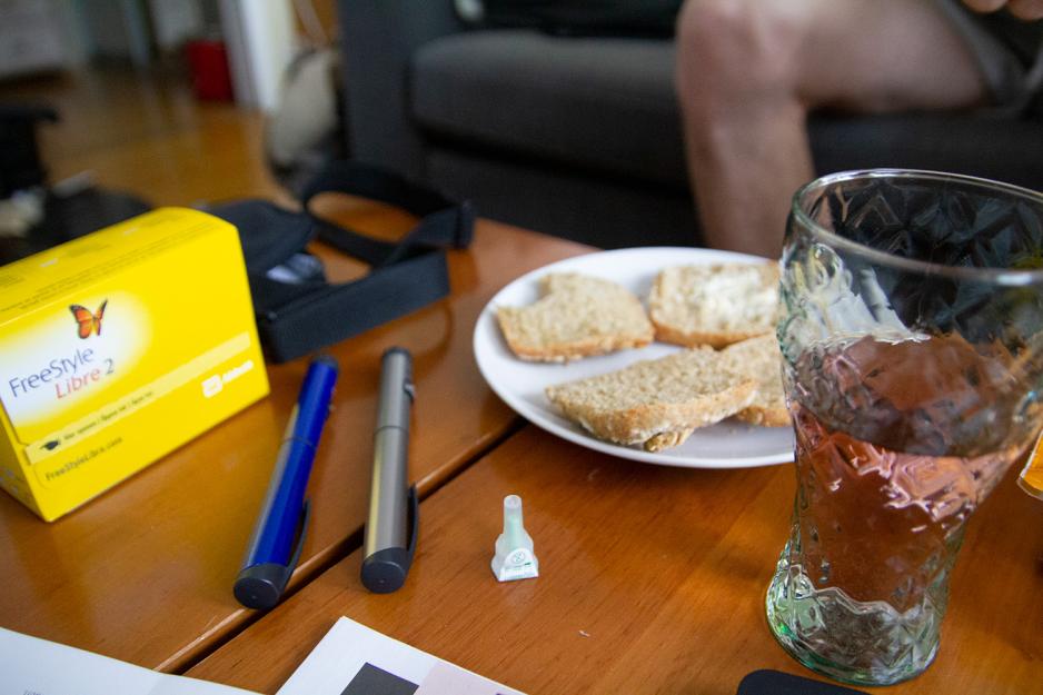 P&aring; et brunt bord ligger det to insulinpenner. Ved siden av st&aring;r et glass saft og rundstykker p&aring; en tallerken. 