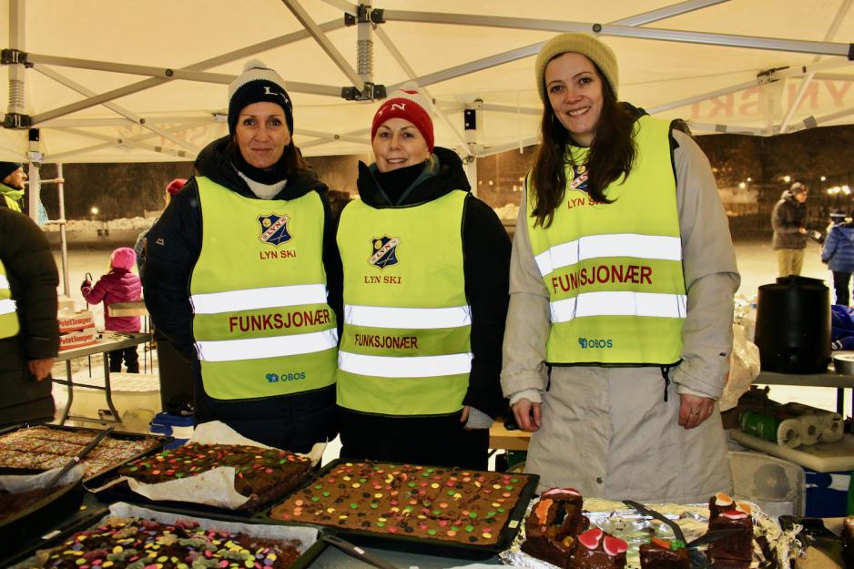 Tre damer st&aring;r foran et kakebord p&aring; et skirenn.