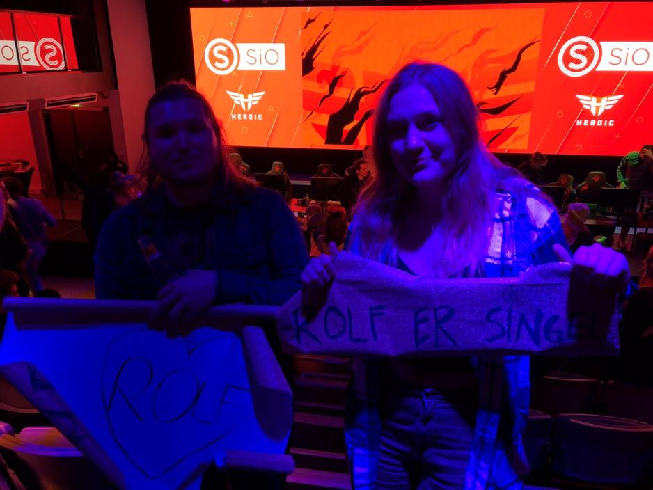 To personer smiler til kamera og holder plakater som heier p&aring; laget "Rolf er singel"