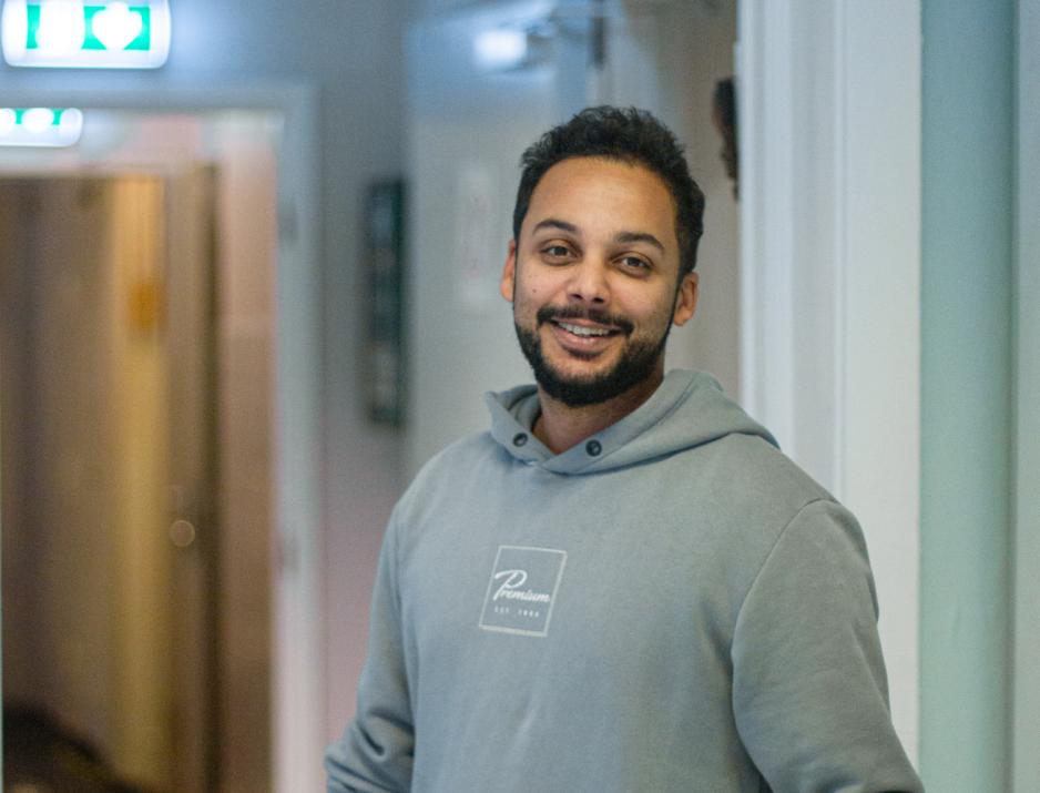 Tim Sarr i gangene til Dragen fritidsklubb. Smilende og ikled bl&aring; genser.