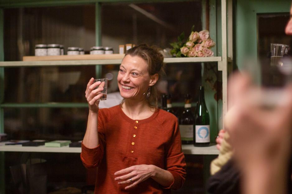 Fr&oslash;ydis sk&aring;ler til menneskene som kom p&aring; &aring;pningen til det nye lokalet. Hun er ikledd en r&oslash;d topp fra Fogg og smiler. Man ser glass i forgrunnen av bildet, og hyller i bakgrunnen.
