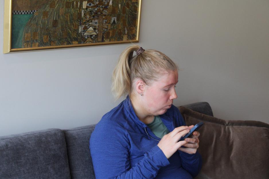 Kristin Hauglid sitter i sofaen, med telefonen n&aelig;rme ansiktet. Hun justerer hastigheten p&aring; p&aring; skjermleseren p&aring; telefonen.