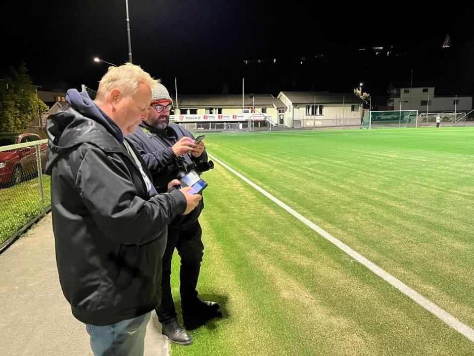 Marius Helg&aring; og Trond S&aelig;ter&oslash;y noterer p&aring; mobiltelefonene langs sidelinja. Banen er i bakgrunnen.