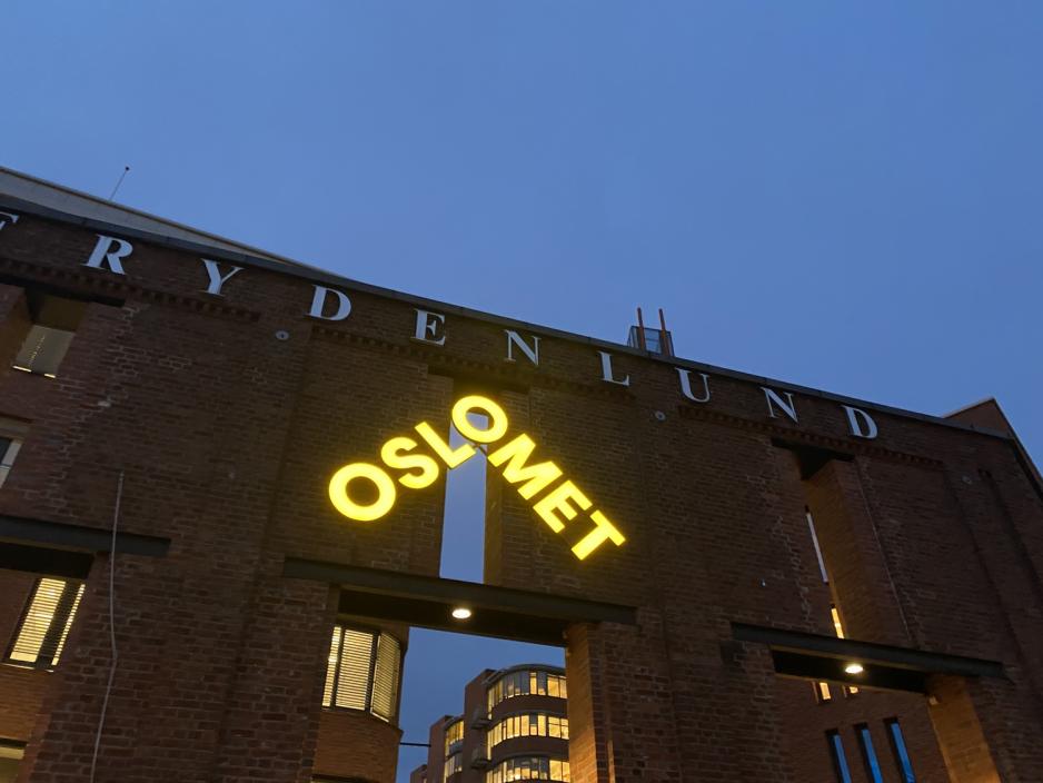 Det lysende gule OsloMet-skiltet p&aring; Frydenlund i m&oslash;rket.