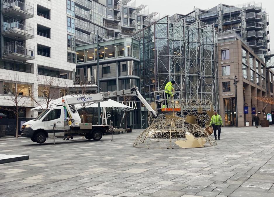 Den digre gule julekulen midt p&aring; torget rives ned av to menn i neongr&oslash;nne jakker. 