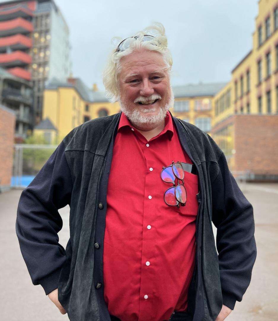 Runar Molstad med et stort smil. Lett hvitt skjegg og mellom langt hvit b&oslash;lgete h&aring;r. R&oslash;d skjorte med svart jakke. 