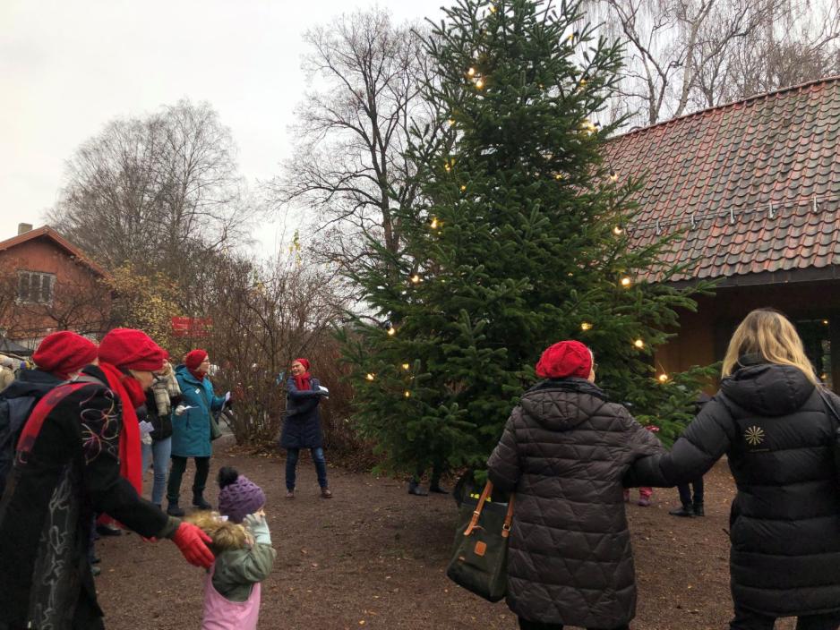 Personer g&aring;r i ring rundt juletreet