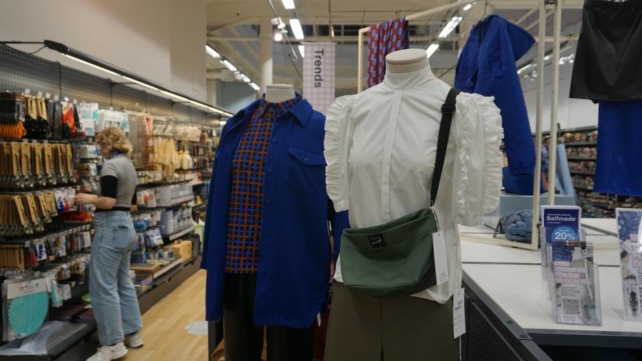 To mannekenger med ulike antrekk p&aring;. En jente i bakgrunnen som ser p&aring; produkter som henger p&aring; hylle.