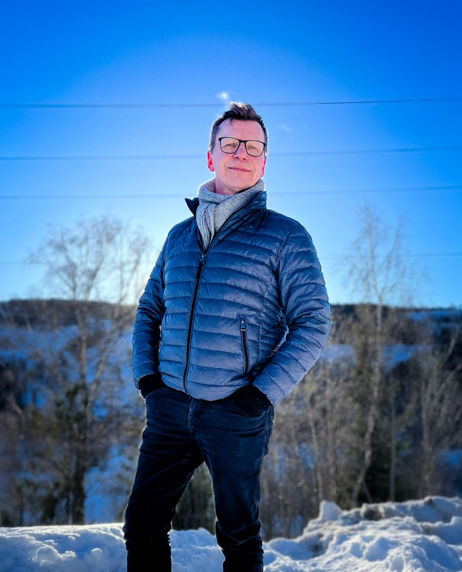 En mann st&aring;r ute i kaldv&aelig;ret foran en h&oslash;ytspennt ledning med skog i bakgrunn