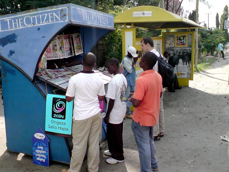 Fem menn st&aring;r rundt en avisstand for The Citizen i Tanzania. 