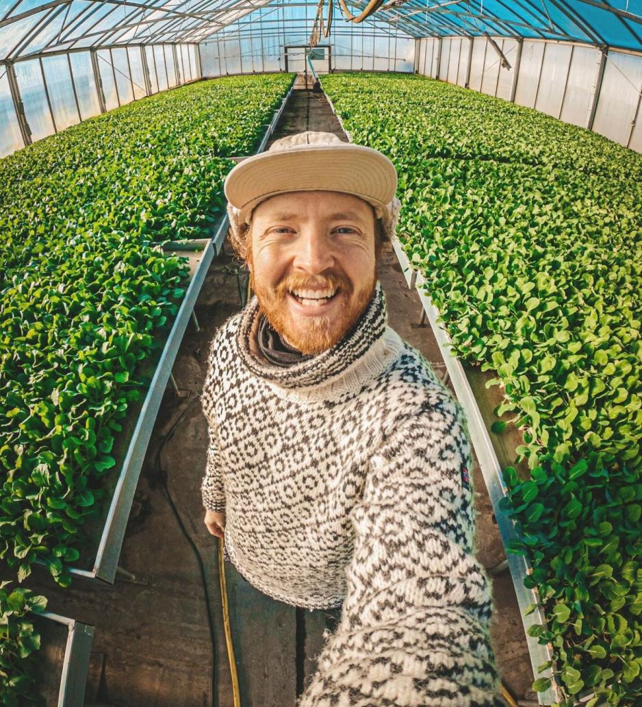 En mann smiler mot kamera, bak seg har han masse gr&oslash;nne planter. 