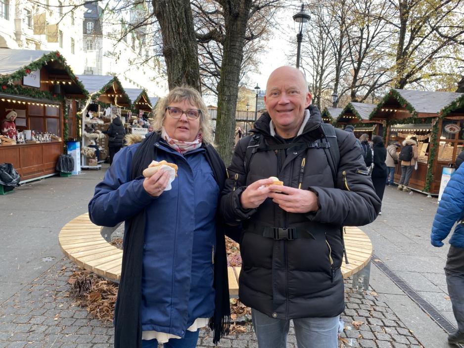 Et dansk ektepar st&aring;r og spiser p&oslash;lser p&aring; et julemarked p&aring; Karl Johan. 
