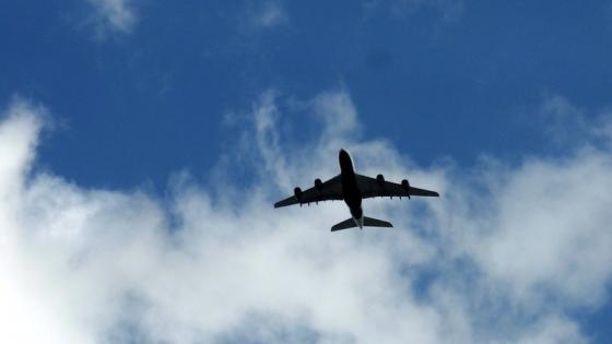Bilde av et fly tatt underfra, bl&aring; himmel og skyer i bakgrunnen.