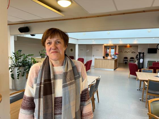 Dame med skjerf, smiler, st&aring;r i en kantine