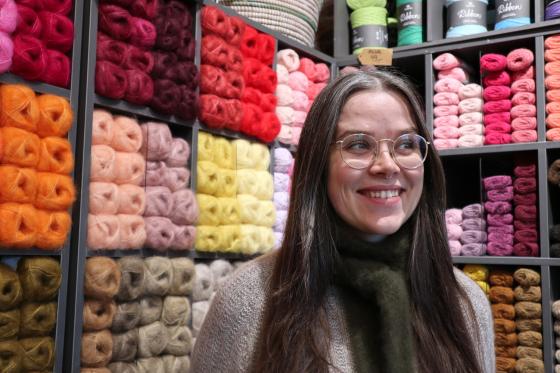 Dame som st&aring;r foran en vegg av garn og smiler