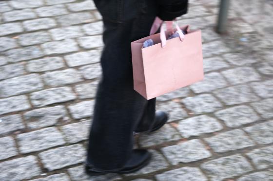 Person som g&aring;r p&aring; fortauet med en rosa papirpose i h&aring;nden.