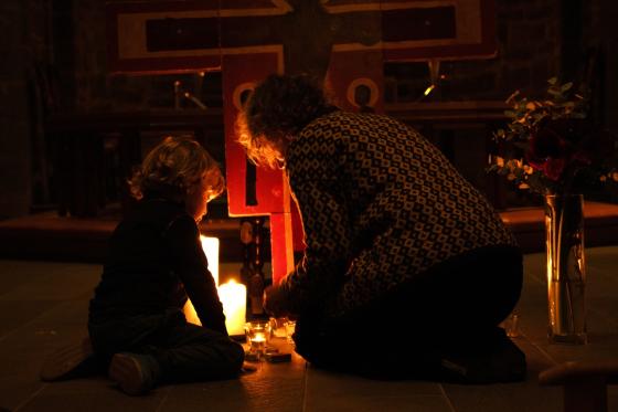 Et barn tenner lys med bestemor foran korset i Gamle Aker kirke.
