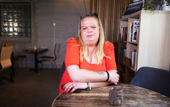Portrett av en kvinne p&aring; en cafe. Hun sitter ved et bord med armene liggende p&aring; bordet.