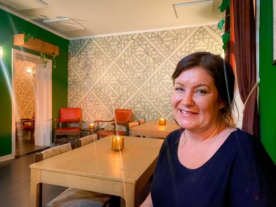 Ei smilende dame st&aring;r p&aring; en sofa og har p&aring; seg en svart t-skjorte. 