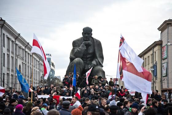 Mange demonstranter som b&aelig;rer p&aring; hviterusslands hvite og r&oslash;de flagg. De er vendt med ryggen mot kameraet og ser p&aring; en st&aring;lstatue av Lenin.
