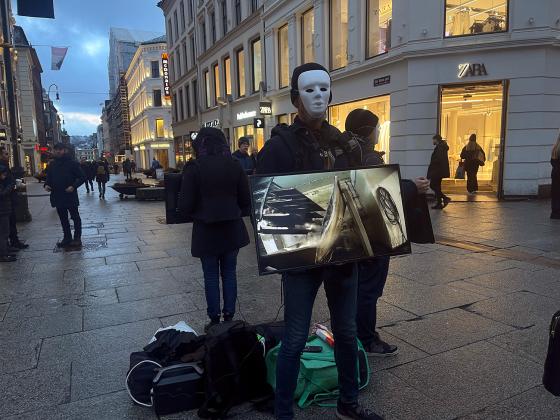 En mann med maske holder en tv-skjerm som viser videoer av dyr som blir mishandlet og slaktet p&aring; norske g&aring;rder 