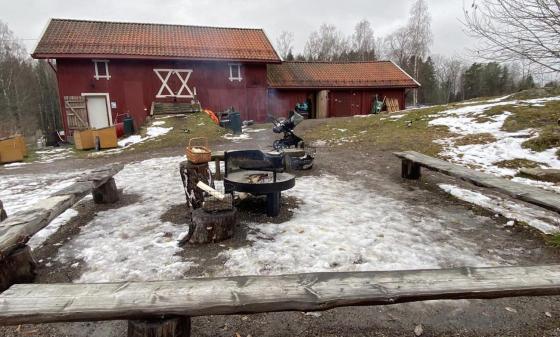 R&oslash;dt g&aring;rdsbruk om vinteren. Tre benker i front av bildet til &aring; sitte p&aring;, med et b&aring;l med r&oslash;yk i midten