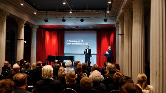 Mann st&aring;r p&aring; scene for &aring; presentere vinnere av gr&oslash;ssmedaljen